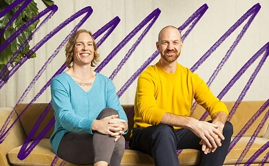 Two people sitting side by side smiling while sitting on a yellow couch
