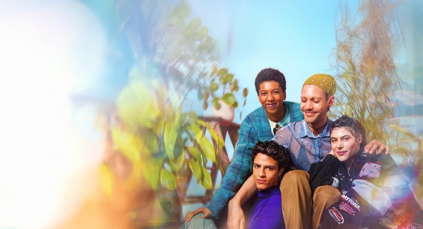 Group of four friends smiling and sitting closely together in a cozy, plant-filled setting