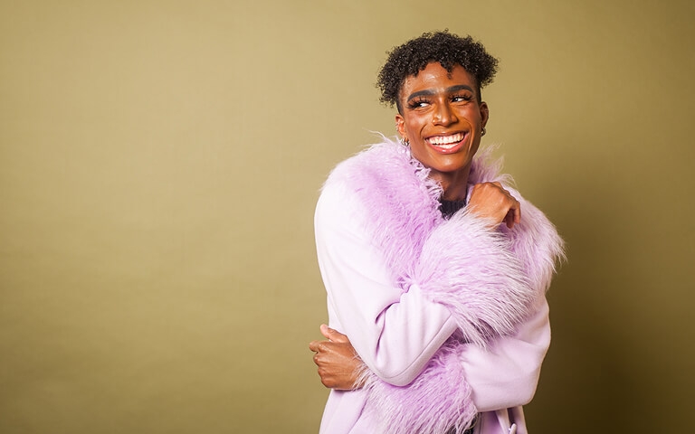 Person smiling wearing a light purple coat against an olive green background