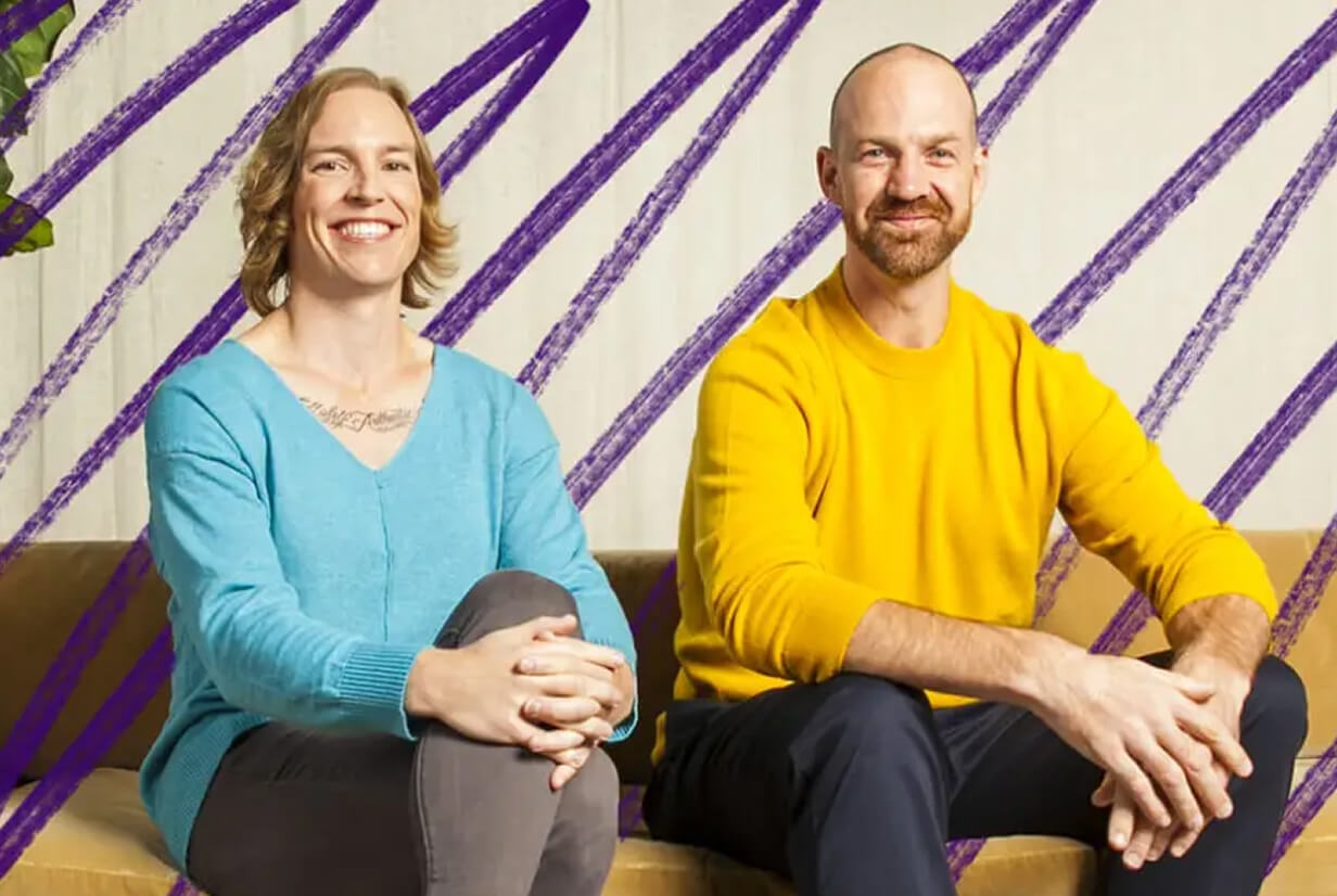 Two people sitting side by side smiling while sitting on a yellow couch
