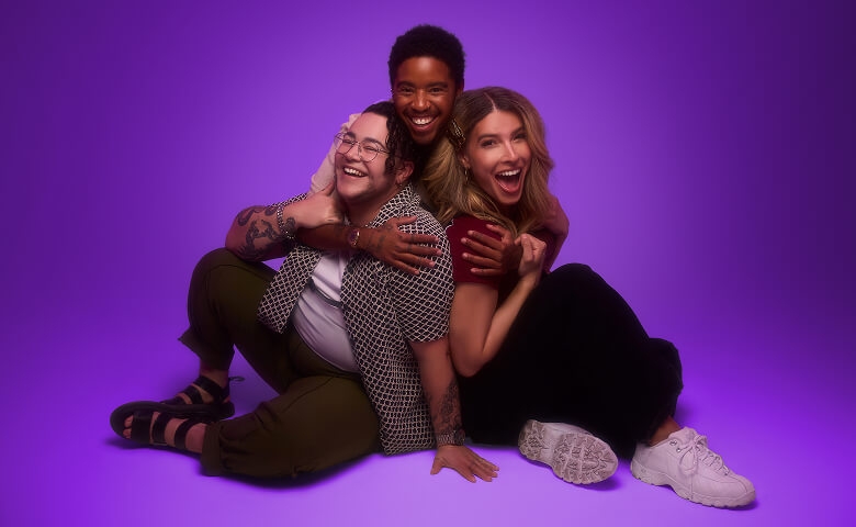 Three diverse and happy friends smile and embrace in front of a purple background